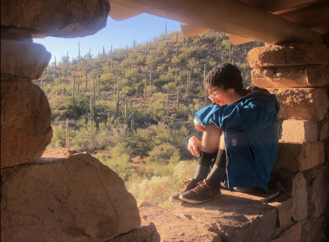 Person sitting on rocks, knees to their chest, looking outward at a view 